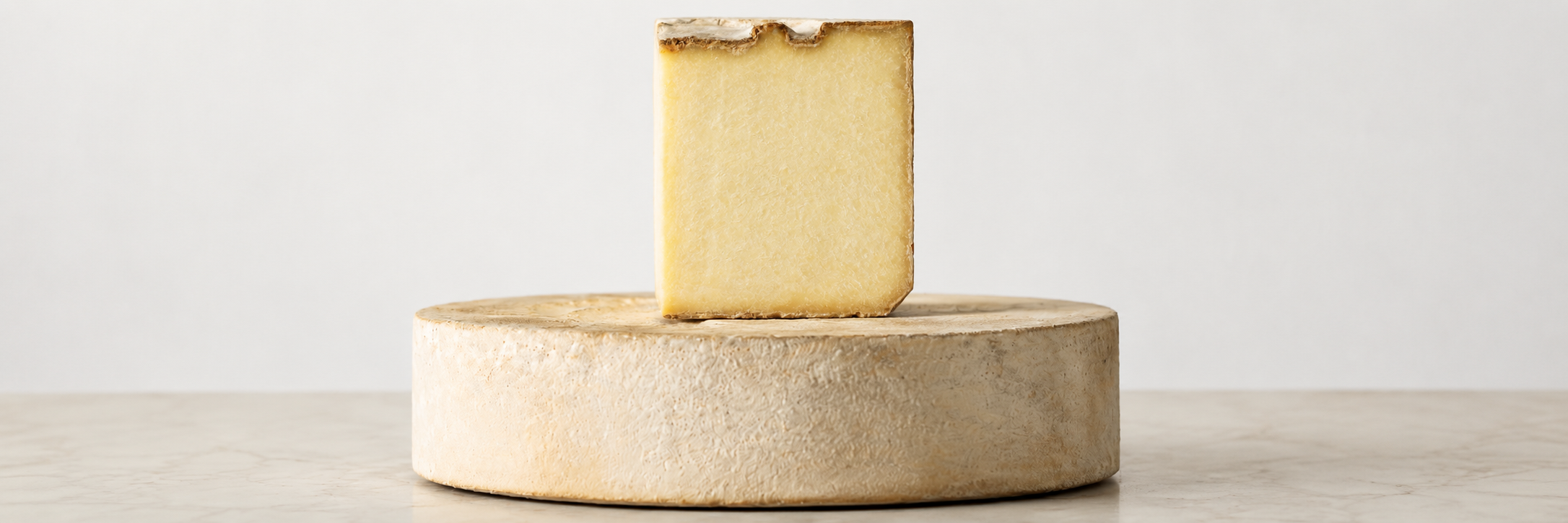 Forma intera di Castelmagno DOP con crosta naturale rugosa, su cui è appoggiata una fetta tagliata che mostra la pasta compatta di colore giallo paglierino.
